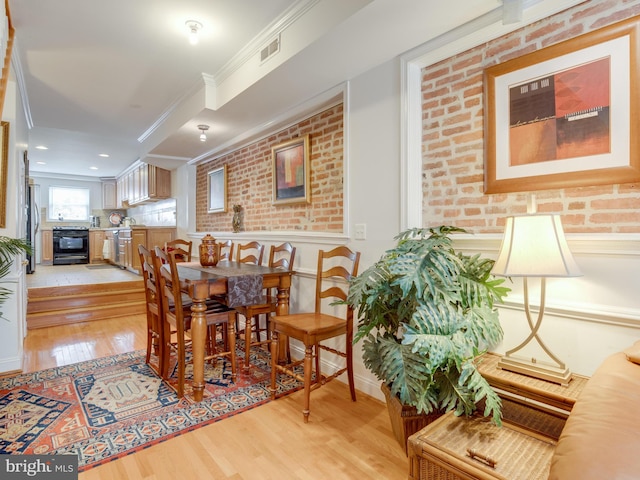 dining room with light hardwood / wood-style floors, ornamental molding, and brick wall