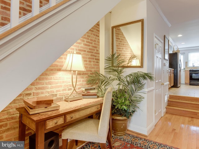 hallway featuring light hardwood / wood-style flooring, brick wall, and ornamental molding