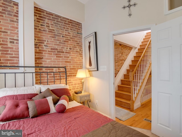 bedroom featuring wood-type flooring and brick wall