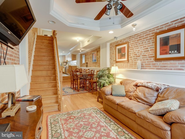 living room with light wood-type flooring, a raised ceiling, crown molding, and brick wall