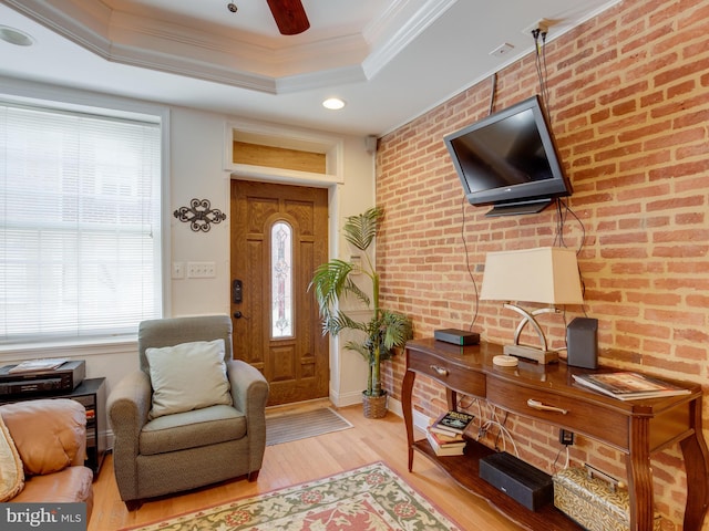 interior space featuring a tray ceiling, ornamental molding, brick wall, and light hardwood / wood-style flooring