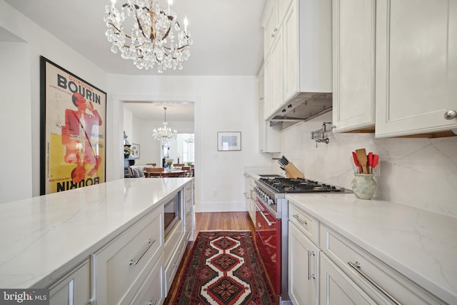 kitchen featuring custom exhaust hood, light stone countertops, appliances with stainless steel finishes, a notable chandelier, and white cabinetry