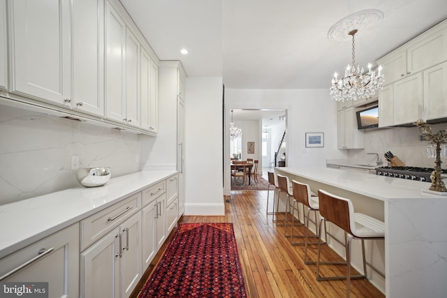 kitchen with decorative backsplash, sink, decorative light fixtures, white cabinets, and light hardwood / wood-style floors