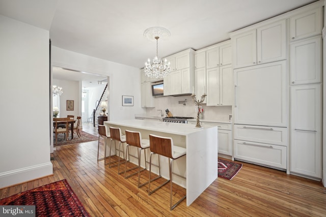 kitchen featuring white cabinetry, light hardwood / wood-style floors, a kitchen island, hanging light fixtures, and a breakfast bar area