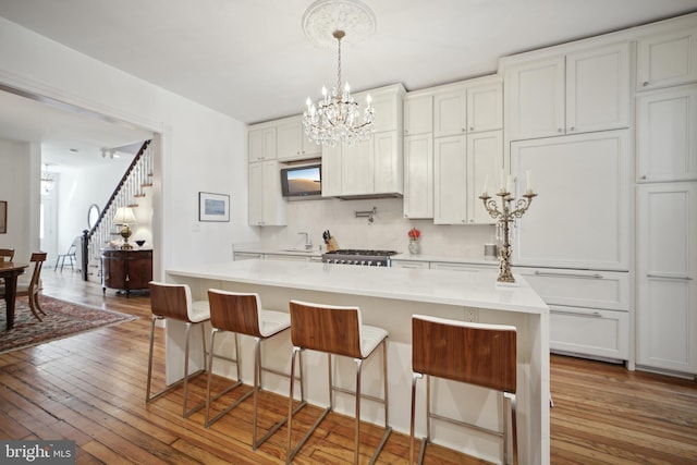 kitchen featuring a kitchen island, wood-type flooring, decorative light fixtures, a breakfast bar, and white cabinets