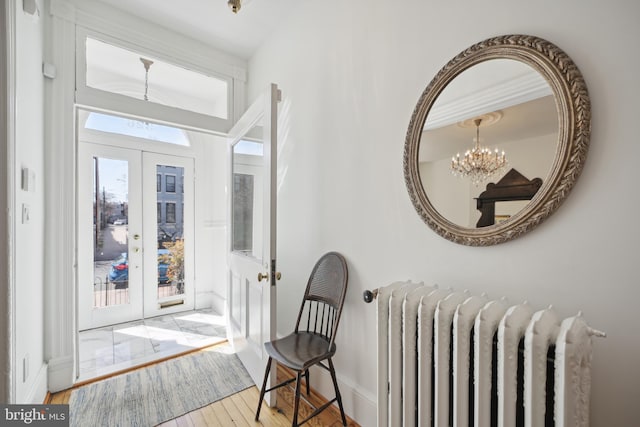 entryway featuring radiator, light hardwood / wood-style flooring, french doors, and an inviting chandelier