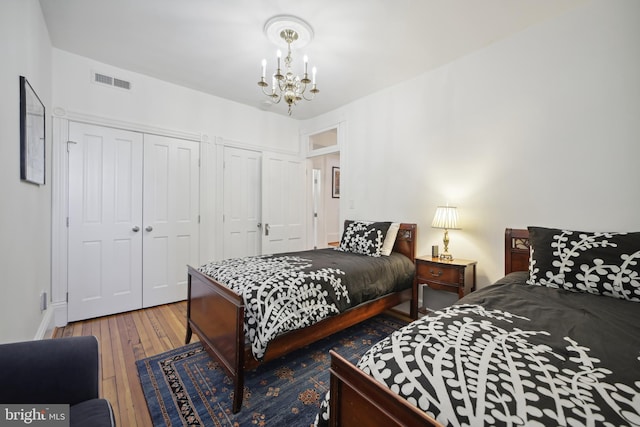 bedroom featuring multiple closets, a chandelier, and hardwood / wood-style flooring