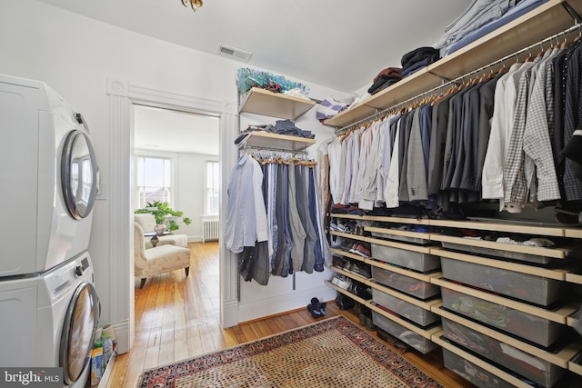 spacious closet featuring stacked washer and dryer, wood-type flooring, and radiator heating unit