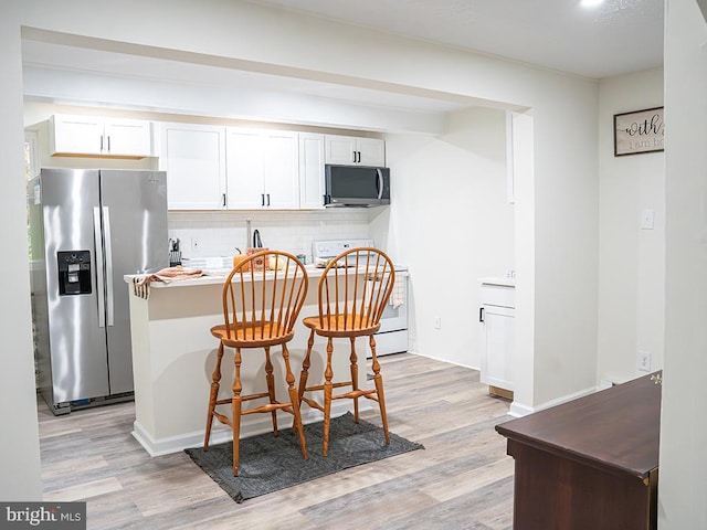 kitchen with a kitchen bar, white cabinetry, light hardwood / wood-style flooring, and appliances with stainless steel finishes