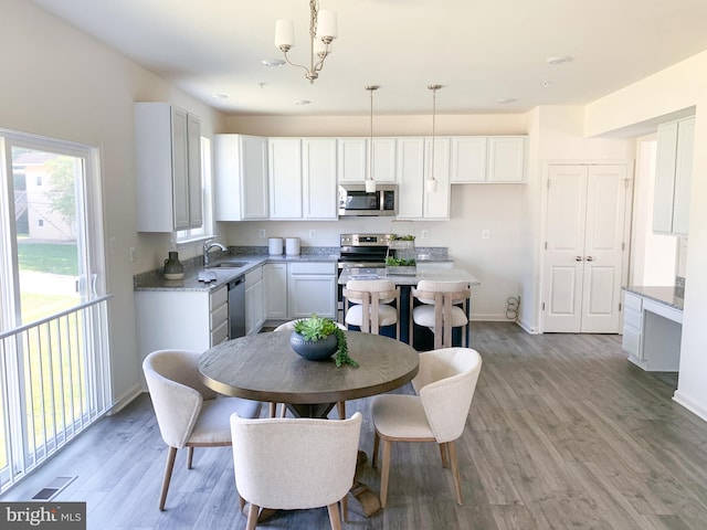 kitchen with light hardwood / wood-style floors, stainless steel appliances, decorative light fixtures, white cabinets, and a chandelier