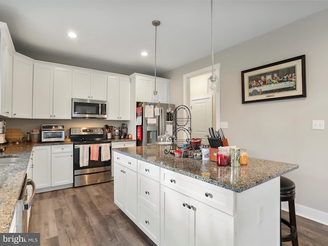 kitchen featuring hanging light fixtures, stainless steel appliances, dark hardwood / wood-style flooring, a center island with sink, and white cabinets