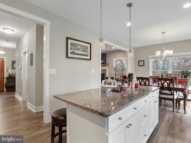 kitchen with wood-type flooring, decorative light fixtures, dark stone countertops, white cabinets, and a center island