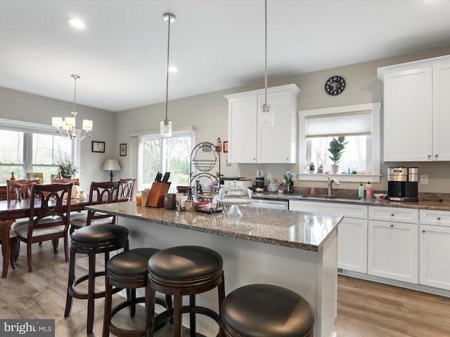 kitchen with white cabinetry, light hardwood / wood-style flooring, a kitchen island, and decorative light fixtures