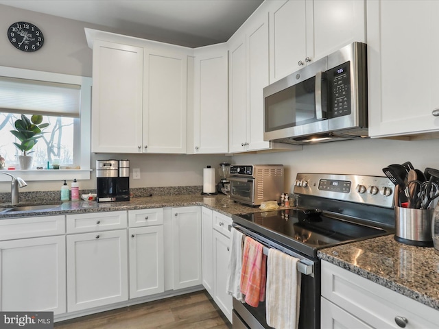 kitchen with appliances with stainless steel finishes, sink, dark stone countertops, white cabinets, and light hardwood / wood-style floors