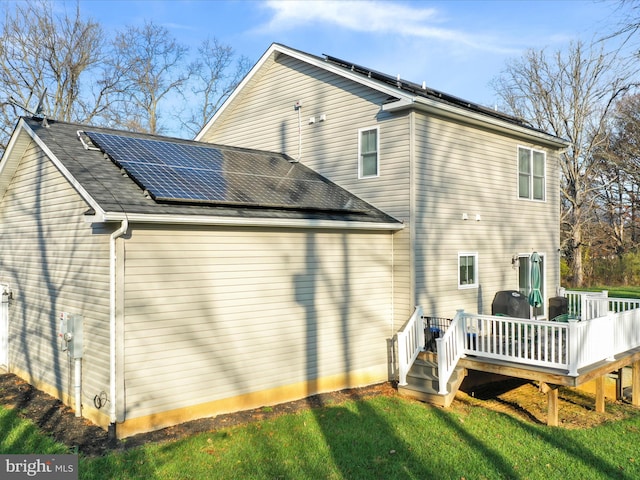 back of property featuring a wooden deck, a yard, and solar panels