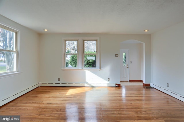 empty room with a textured ceiling, light wood-type flooring, baseboard heating, and a wealth of natural light