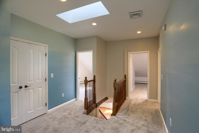 hallway with baseboard heating, light carpet, and a skylight