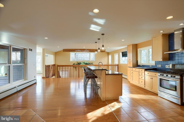 kitchen featuring wall chimney range hood, a kitchen island with sink, stainless steel gas stove, and plenty of natural light