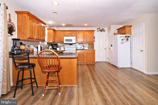 kitchen featuring dark hardwood / wood-style flooring, kitchen peninsula, white appliances, a kitchen bar, and decorative backsplash