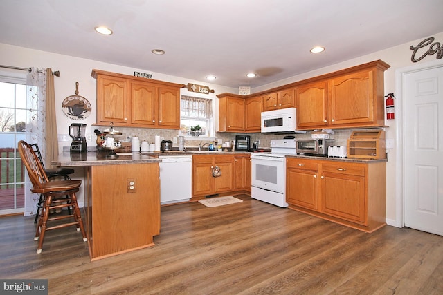 kitchen featuring kitchen peninsula, dark hardwood / wood-style flooring, tasteful backsplash, white appliances, and a breakfast bar area