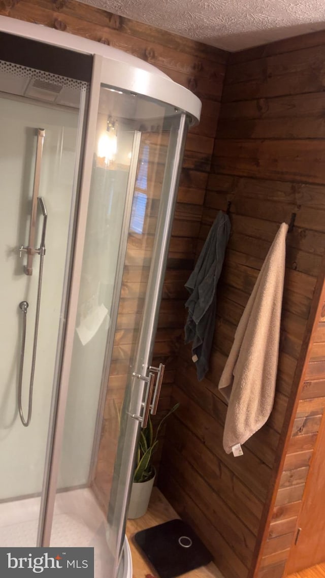 bathroom with a textured ceiling, wood walls, and walk in shower