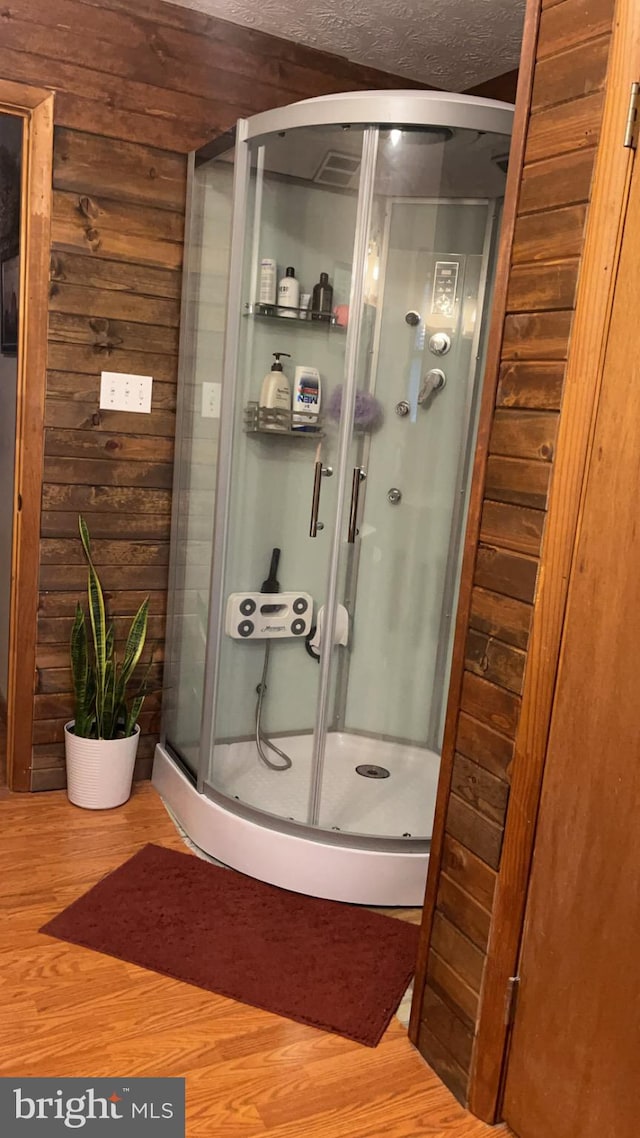 bathroom with wood-type flooring, a textured ceiling, an enclosed shower, and wooden walls