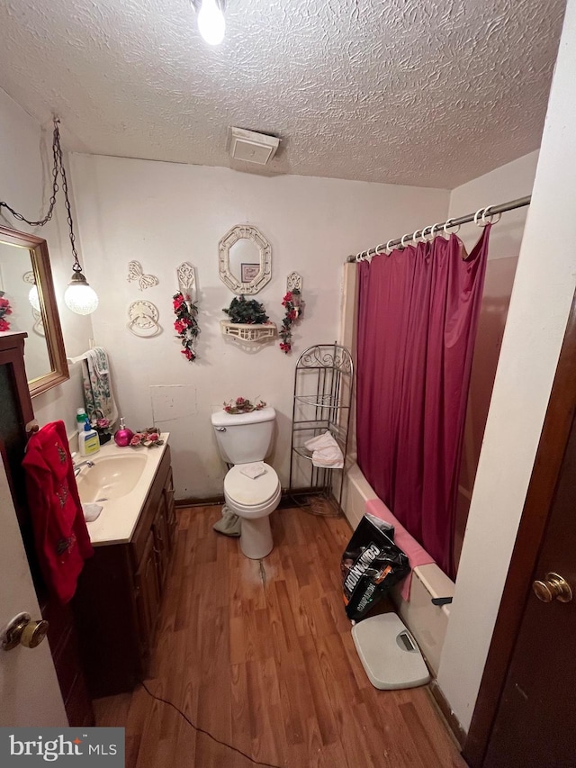 full bathroom featuring hardwood / wood-style flooring, vanity, shower / bath combo with shower curtain, and a textured ceiling