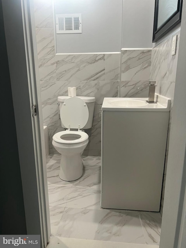 bathroom featuring vanity, tile walls, and toilet