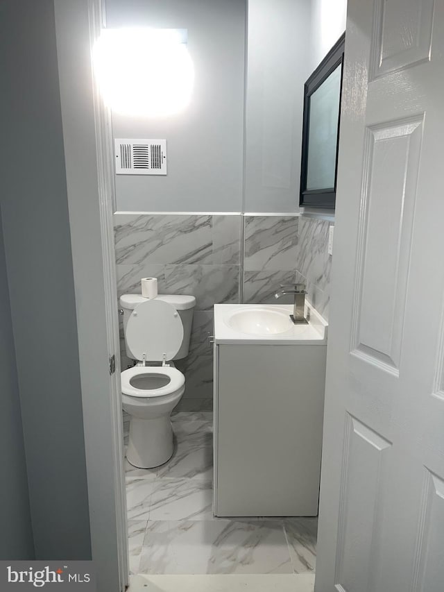 bathroom featuring vanity, toilet, and tile walls