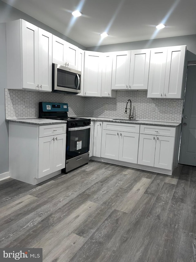 kitchen with white cabinets, dark wood-type flooring, appliances with stainless steel finishes, and tasteful backsplash