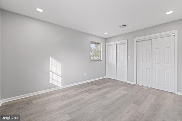 unfurnished bedroom featuring two closets and light hardwood / wood-style flooring