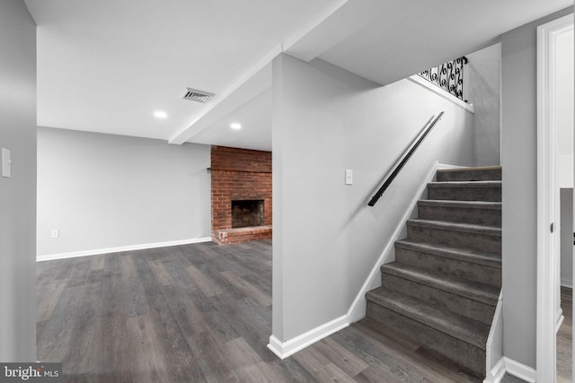 staircase featuring wood-type flooring and a brick fireplace