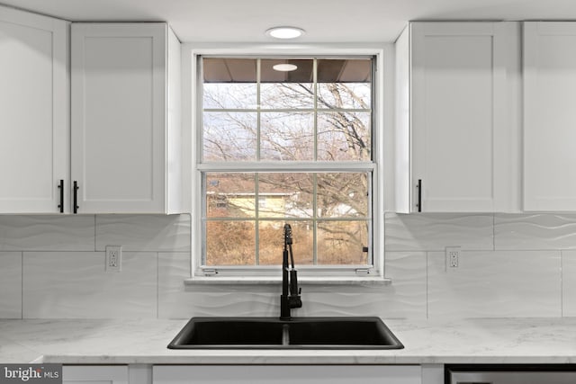 kitchen featuring a wealth of natural light, light stone counters, sink, and white cabinets