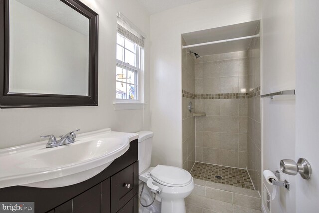 bathroom with tile patterned flooring, toilet, vanity, and tiled shower