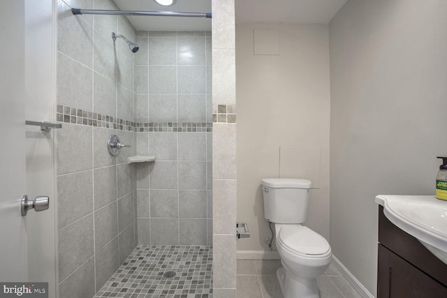 bathroom featuring tile patterned flooring, vanity, toilet, and tiled shower