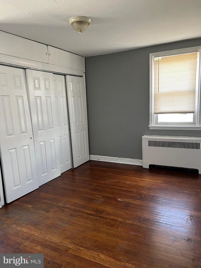 unfurnished bedroom featuring a closet, radiator heating unit, and dark wood-type flooring