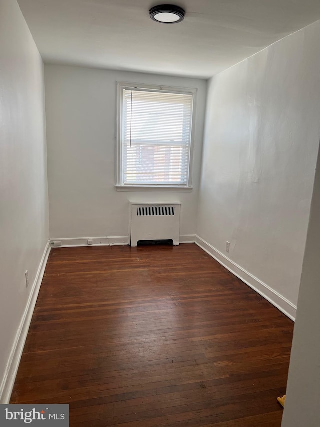 empty room with dark hardwood / wood-style flooring and radiator heating unit