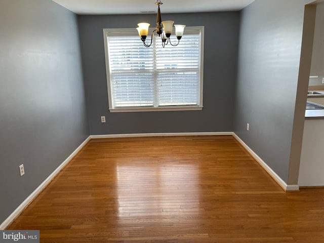 unfurnished dining area with wood-type flooring and a chandelier