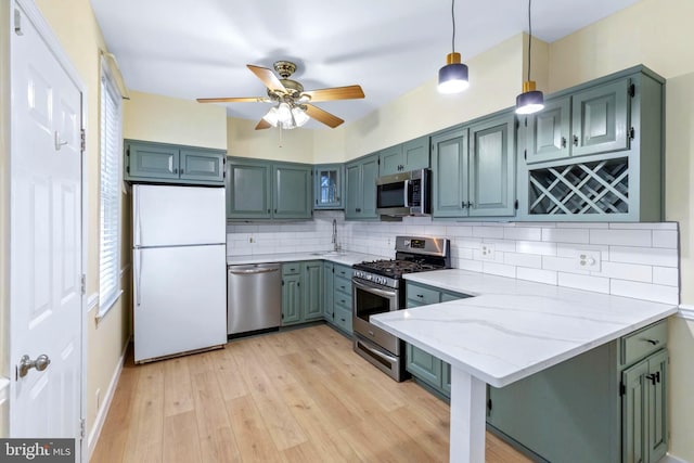 kitchen featuring hanging light fixtures, light stone counters, kitchen peninsula, decorative backsplash, and appliances with stainless steel finishes