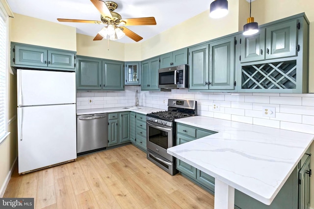 kitchen with light stone counters, backsplash, pendant lighting, appliances with stainless steel finishes, and light wood-type flooring