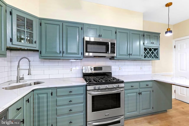 kitchen featuring light stone countertops, stainless steel appliances, sink, light hardwood / wood-style flooring, and hanging light fixtures