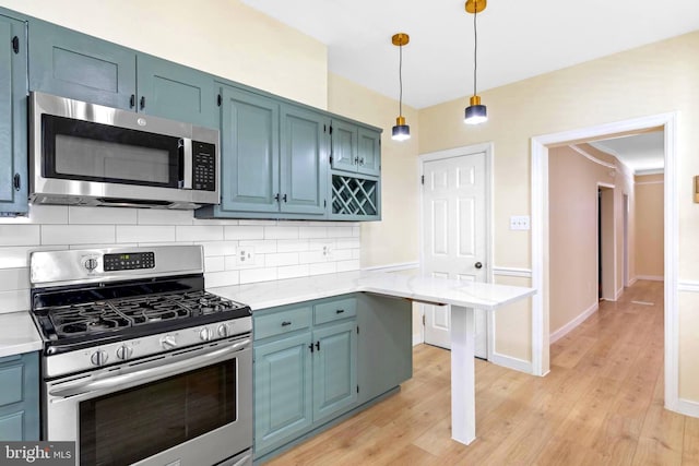 kitchen with tasteful backsplash, hanging light fixtures, light wood-type flooring, and appliances with stainless steel finishes