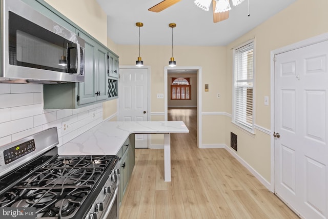 kitchen with hanging light fixtures, stainless steel appliances, light stone counters, backsplash, and light hardwood / wood-style floors