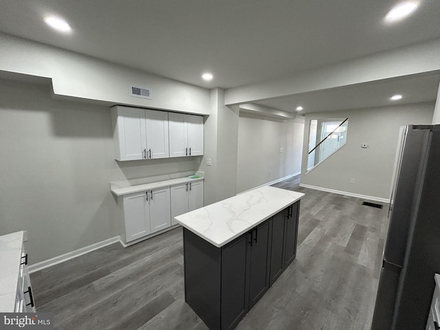 kitchen featuring stainless steel refrigerator, white cabinetry, light stone counters, dark hardwood / wood-style flooring, and a kitchen island