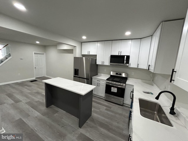 kitchen with hardwood / wood-style floors, light stone counters, white cabinetry, and stainless steel appliances