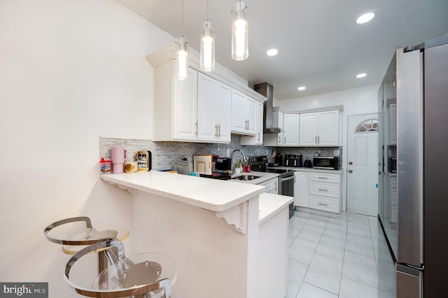 kitchen with kitchen peninsula, a kitchen breakfast bar, appliances with stainless steel finishes, wall chimney range hood, and white cabinets