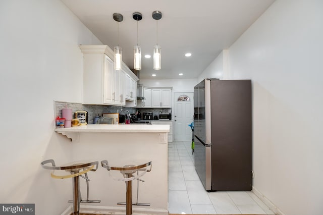 kitchen featuring stainless steel refrigerator, a kitchen breakfast bar, kitchen peninsula, decorative backsplash, and white cabinets