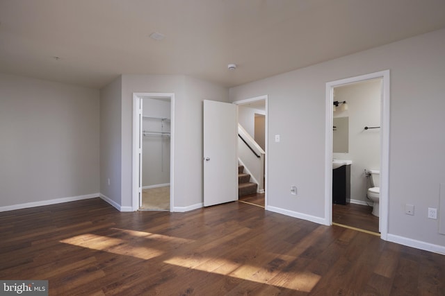 unfurnished bedroom with connected bathroom, a spacious closet, a closet, and dark hardwood / wood-style floors