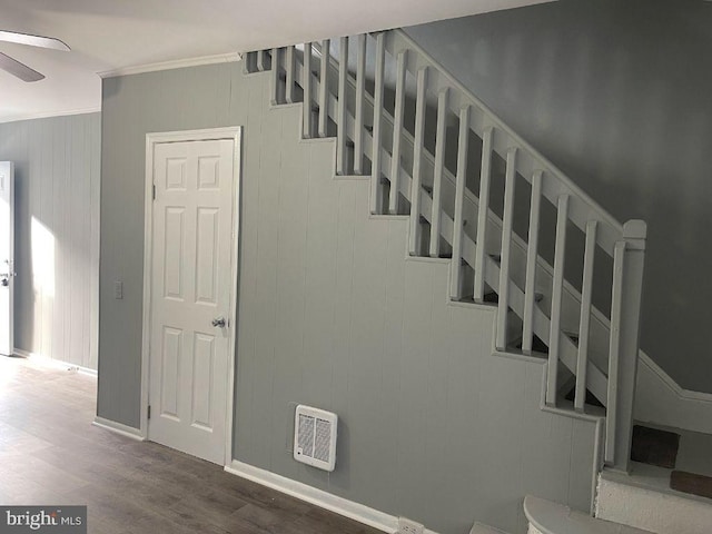 stairs with ceiling fan, hardwood / wood-style flooring, heating unit, wooden walls, and ornamental molding