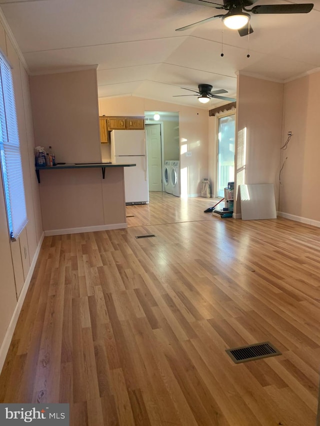 unfurnished living room with ornamental molding, vaulted ceiling, ceiling fan, light hardwood / wood-style flooring, and washing machine and clothes dryer